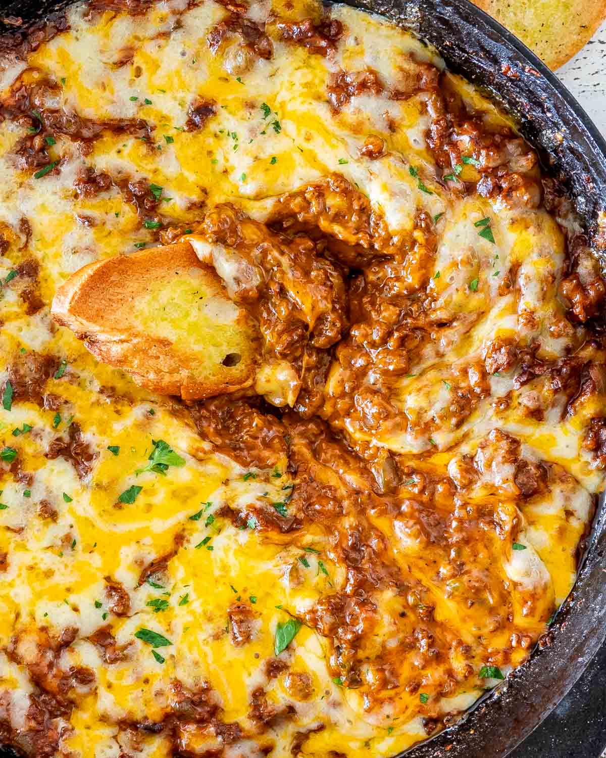 sloppy joe dip in a black skillet with a piece of toasted bread in it.