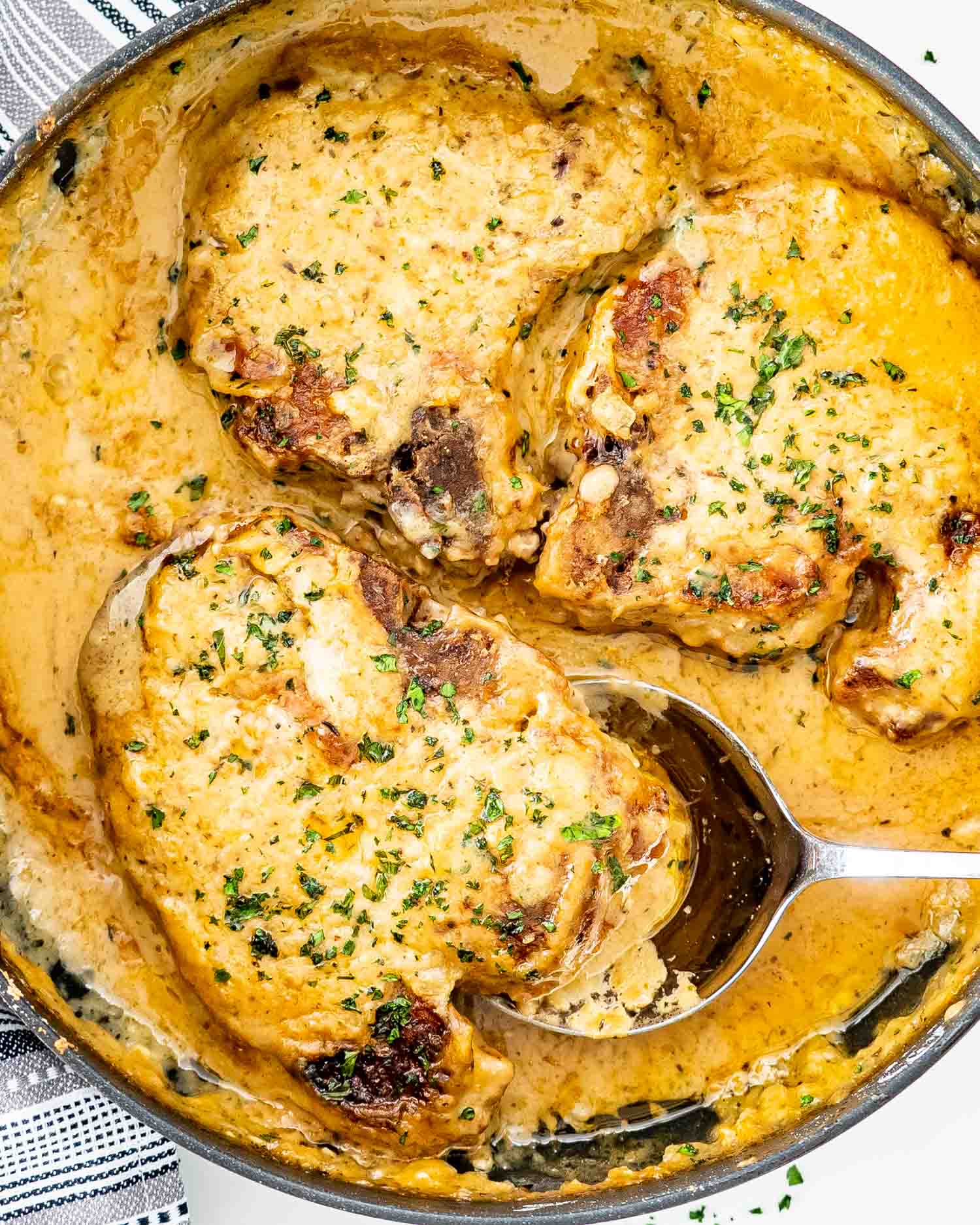 smothered pork chops in a skillet garnished with parsley.