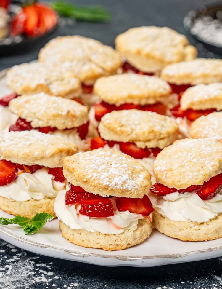 a few strawberry shortcakes on a white platter sprinkled with powdered sugar.
