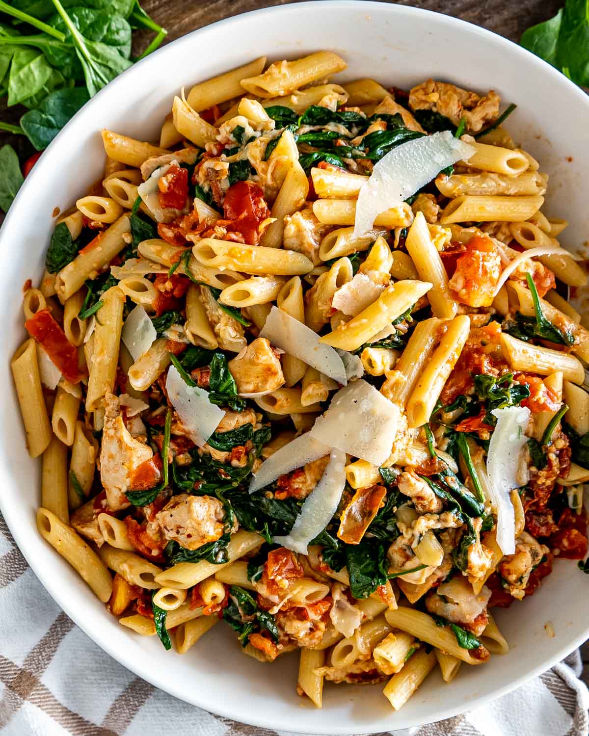 tomato spinach chicken pasta in a white bowl.