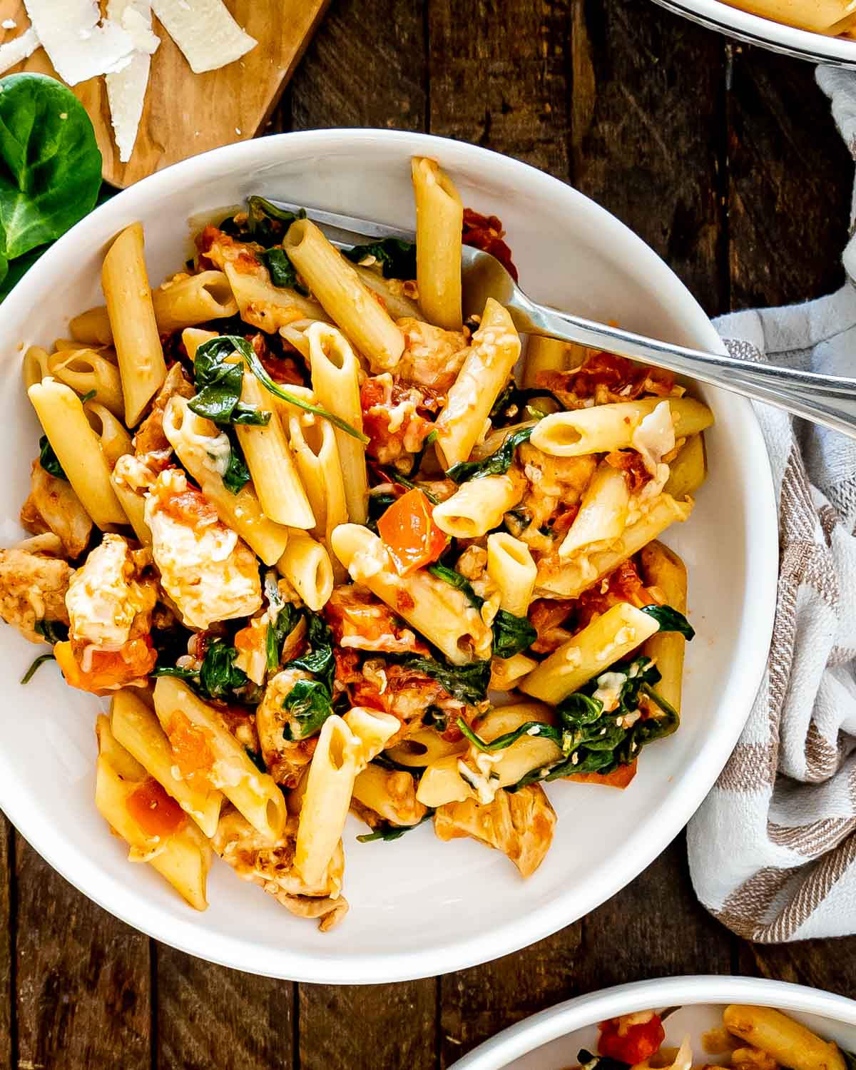 tomato spinach chicken pasta in a white bowl.