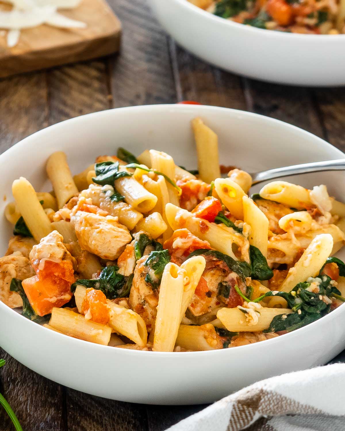 tomato spinach chicken pasta in a white bowl.