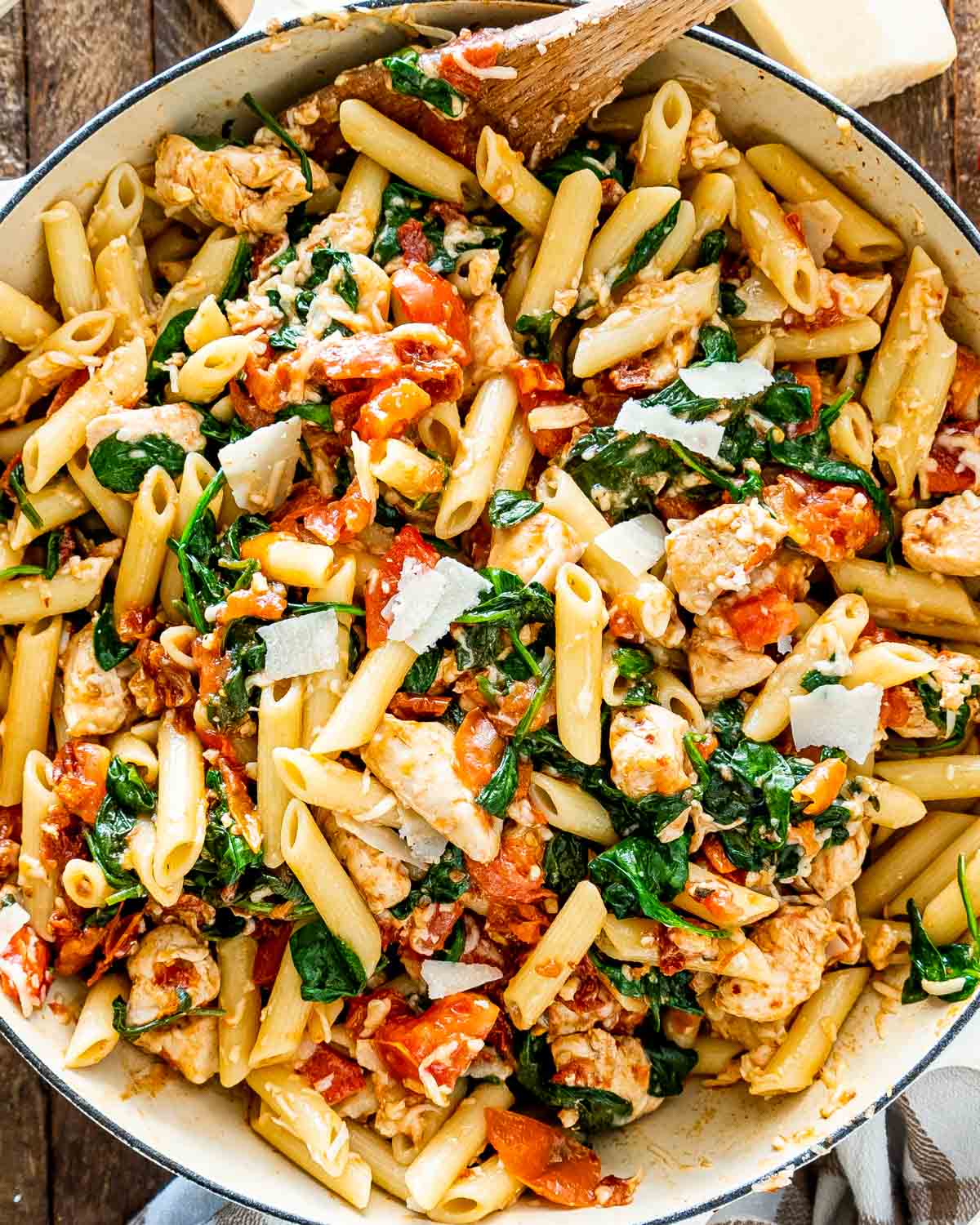 tomato spinach chicken pasta in a white bowl.