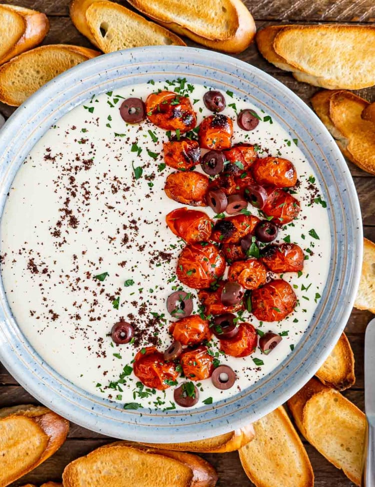 a bowl with whipped feta dip topped with roasted tomatoes surround by pita chips.