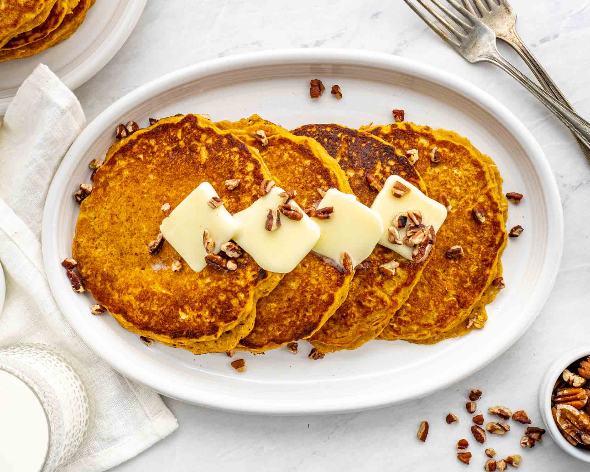 stack of whole wheat pumpkin pancakes on a white plate with pecans and a pat of butter.