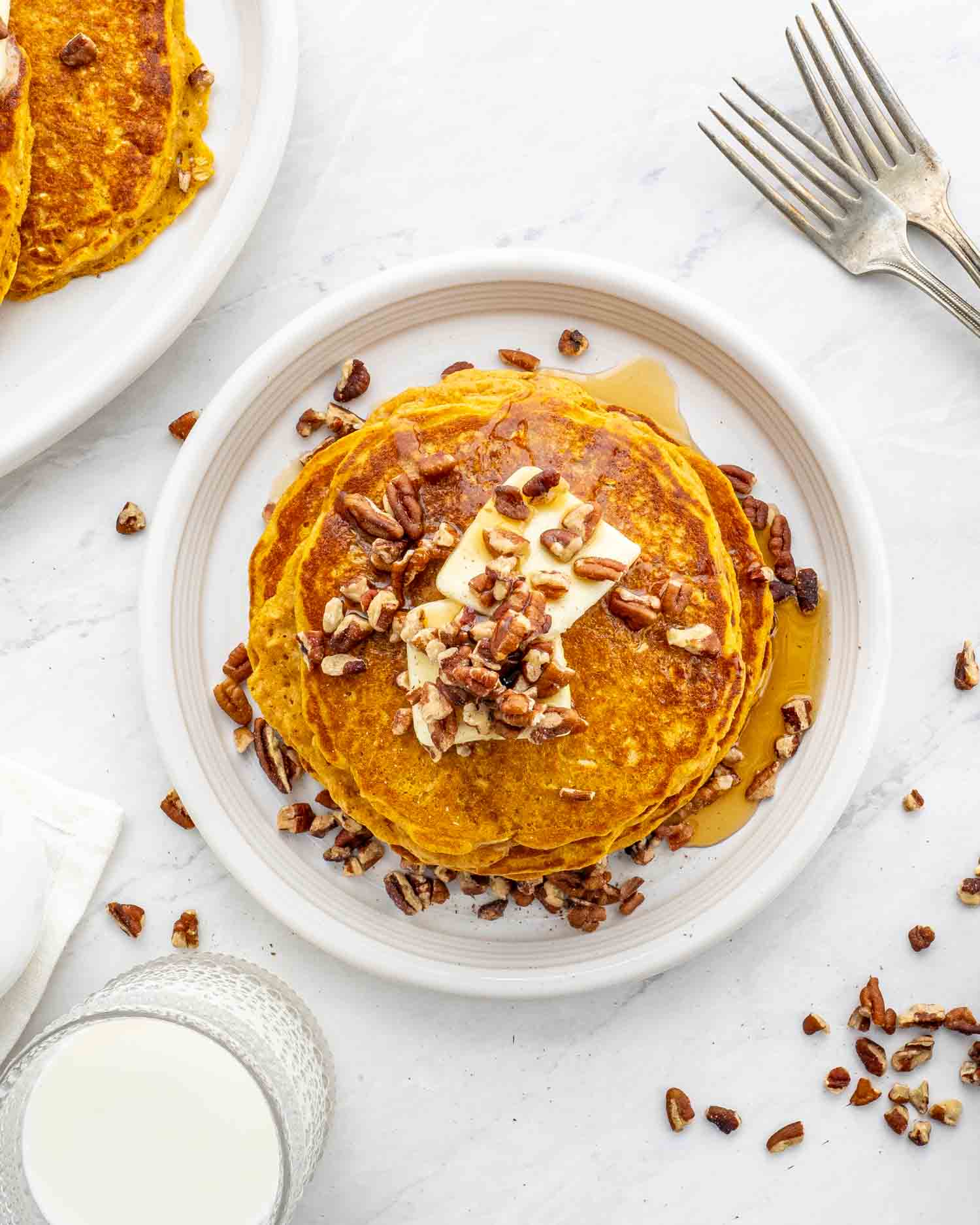 stack of whole wheat pumpkin pancakes on a white plate with pecans and a pat of butter.