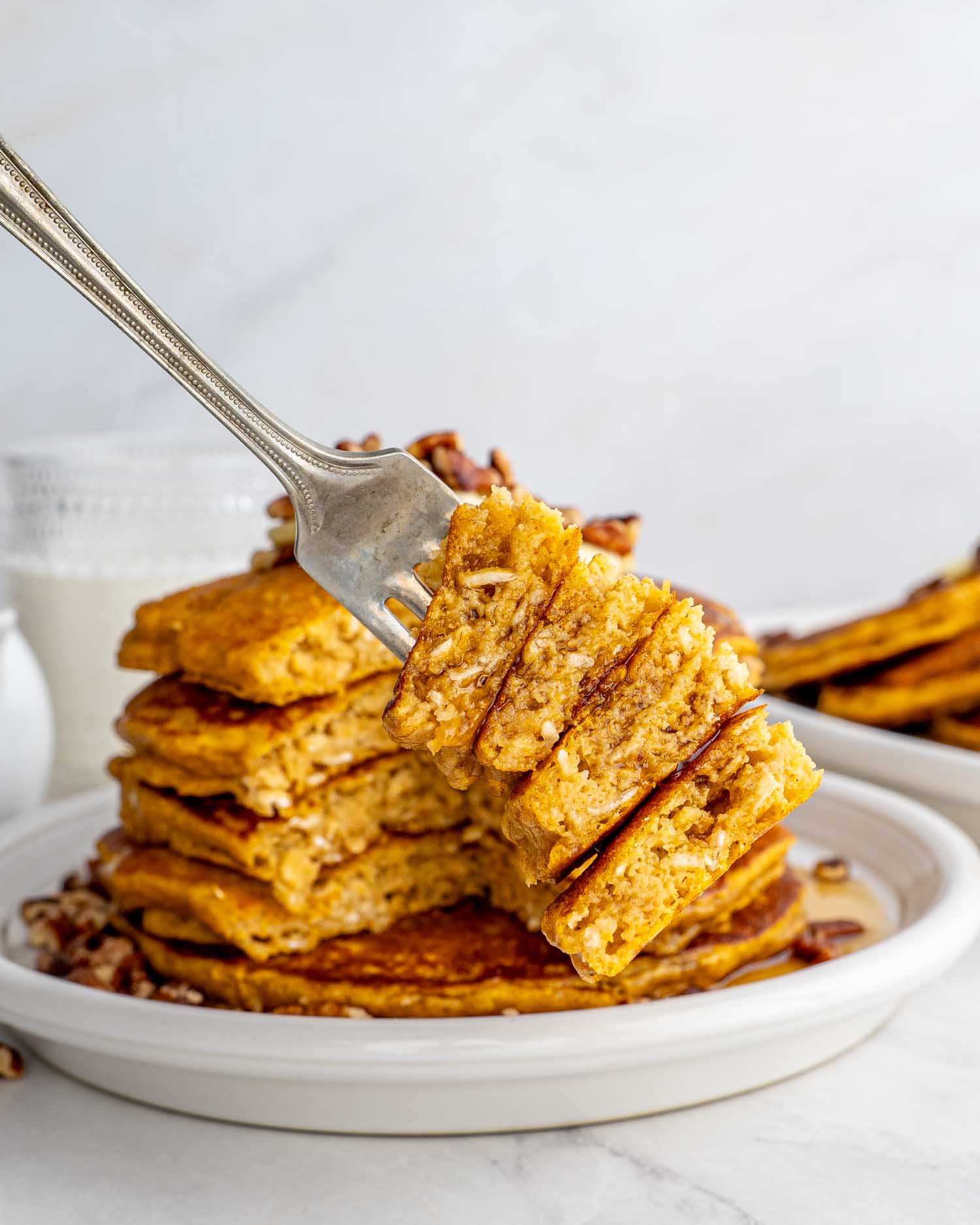 Stack of whole wheat pumpkin pancakes on a plate with a fork taking a piece.